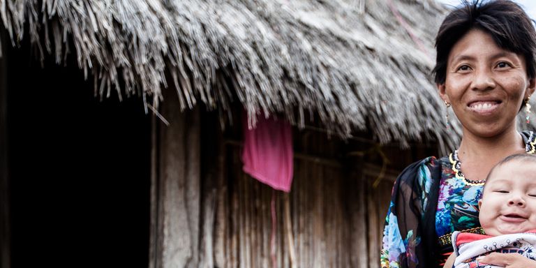 An indigenous woman is carrying her baby in front of a hut - Inter-American Development Bank - IDB